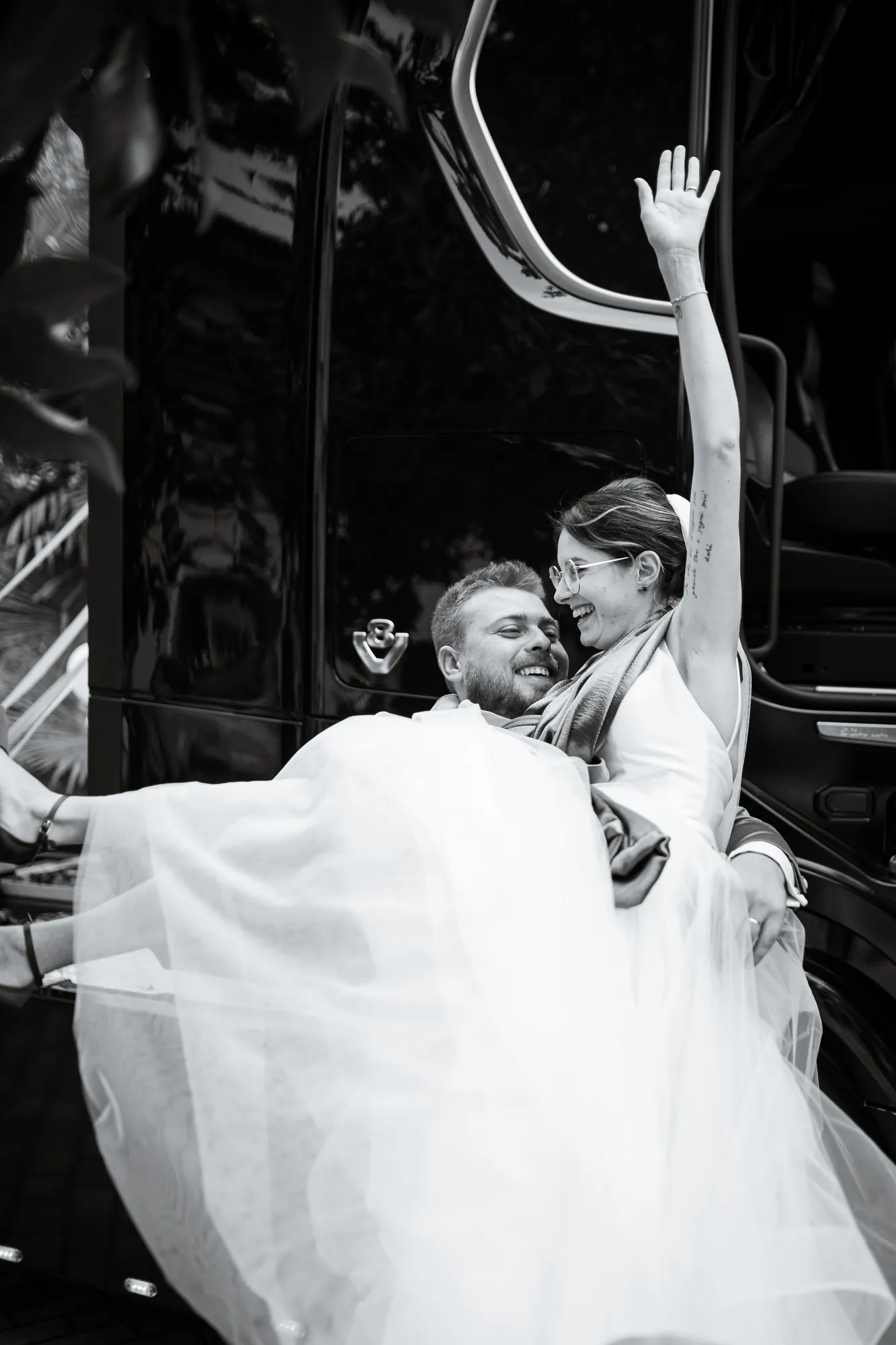 Sposo che solleva la sposa, lei ride con il braccio alzato